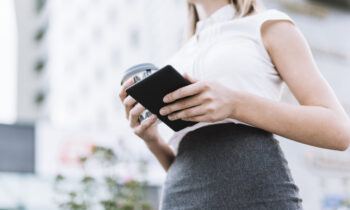 low-angle-view-businesswoman-holding-smartphone-disposable-coffee-cup-outdoors