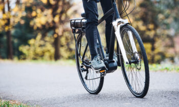 An unrecognizable man on electrobike cycling outdoors on a road in park.