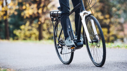 An unrecognizable man on electrobike cycling outdoors on a road in park.